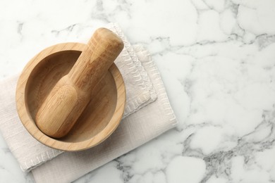 Photo of Wooden mortar, pestle and cloth on white marble table, top view. Space for text