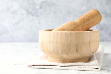 Photo of Wooden mortar, pestle and cloth on white marble table, closeup