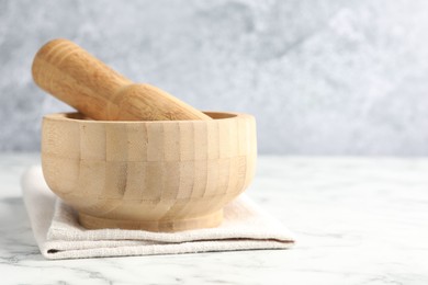 Photo of Wooden mortar, pestle and cloth on white marble table, closeup