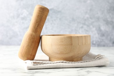 Photo of Wooden mortar, pestle and cloth on white marble table, closeup