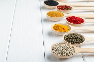 Photo of Different aromatic spices in spoons on white wooden table, closeup. Space for text