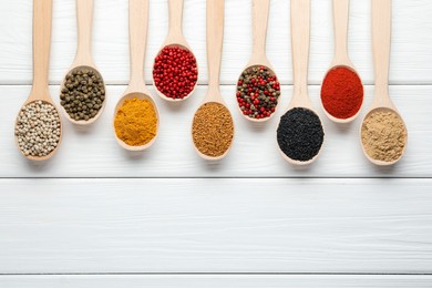 Photo of Different aromatic spices in spoons on white wooden table, flat lay. Space for text