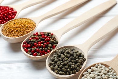 Photo of Different aromatic spices in spoons on white wooden table, closeup