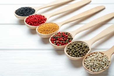 Photo of Different aromatic spices in spoons on white wooden table, closeup