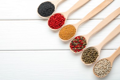Photo of Different aromatic spices in spoons on white wooden table, flat lay. Space for text