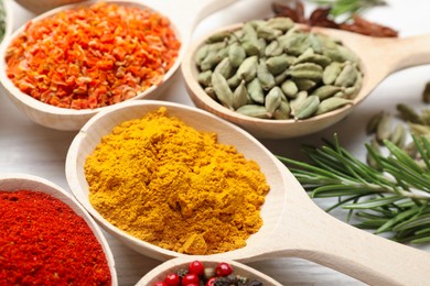 Photo of Different aromatic spices in spoons on white wooden table, closeup