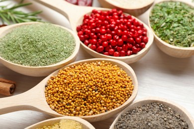 Photo of Different aromatic spices in spoons on white wooden table, closeup