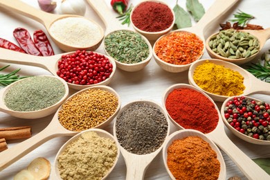 Photo of Different aromatic spices in spoons on white wooden table, closeup