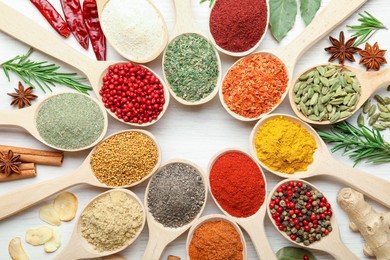 Photo of Different aromatic spices in spoons on white wooden table, flat lay