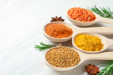 Photo of Different aromatic spices in spoons on white wooden table, closeup. Space for text