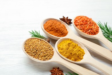 Photo of Different aromatic spices in spoons on white wooden table, closeup