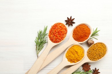 Photo of Different aromatic spices in spoons on white wooden table, flat lay. Space for text