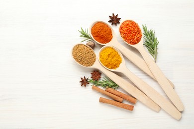 Photo of Different aromatic spices in spoons on white wooden table, flat lay. Space for text