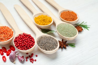 Photo of Different aromatic spices in spoons on white wooden table, closeup