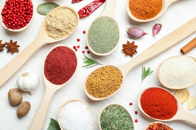 Photo of Different aromatic spices in spoons on white wooden table, flat lay