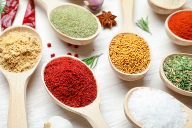 Photo of Different aromatic spices in spoons on white wooden table, closeup
