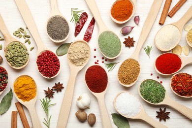 Photo of Different aromatic spices in spoons on white wooden table, flat lay