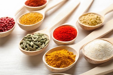 Photo of Different aromatic spices in spoons on white wooden table, closeup