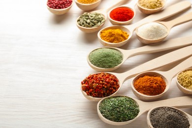 Photo of Different aromatic spices in spoons on white wooden table, closeup. Space for text
