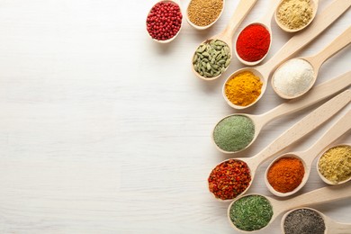 Photo of Different aromatic spices in spoons on white wooden table, flat lay. Space for text