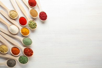 Photo of Different aromatic spices in spoons on white wooden table, flat lay. Space for text