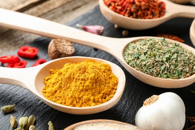 Photo of Different aromatic spices in spoons on wooden table, closeup