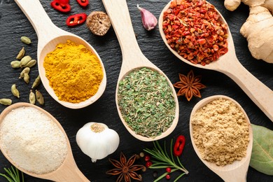 Photo of Different aromatic spices in spoons on black table, closeup