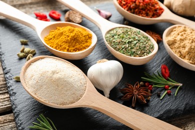 Photo of Different aromatic spices in spoons on wooden table, closeup