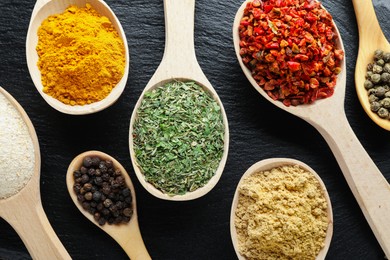 Photo of Different aromatic spices in spoons on black table, closeup
