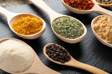 Photo of Different aromatic spices in spoons on black table, closeup