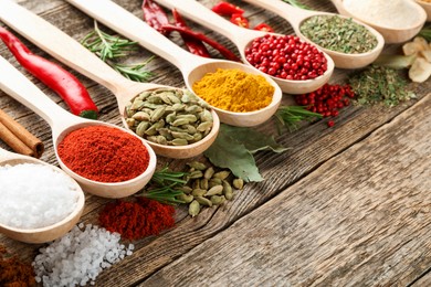 Photo of Different aromatic spices in spoons on wooden table, closeup