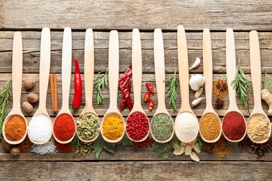 Photo of Different aromatic spices in spoons on wooden table, flat lay
