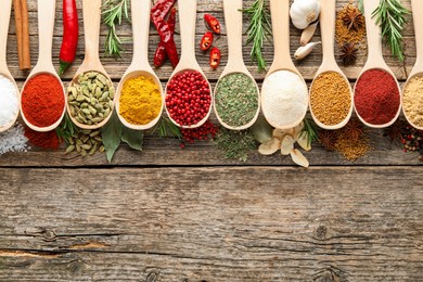 Photo of Different aromatic spices in spoons on wooden table, flat lay. Space for text
