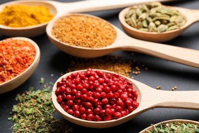 Photo of Different aromatic spices in spoons on black table, closeup