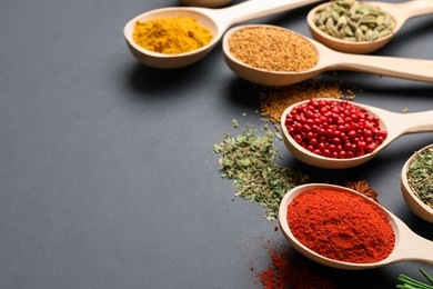 Photo of Different aromatic spices in spoons on black table, closeup. Space for text