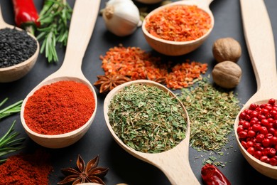 Photo of Different aromatic spices in spoons on black table, closeup