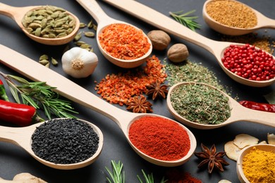 Photo of Different aromatic spices in spoons on black table, closeup