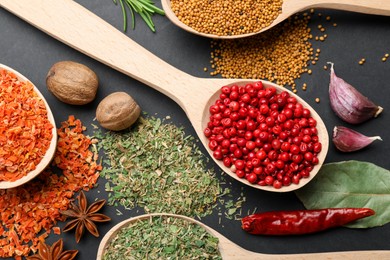 Photo of Different aromatic spices in spoons on black table, flat lay