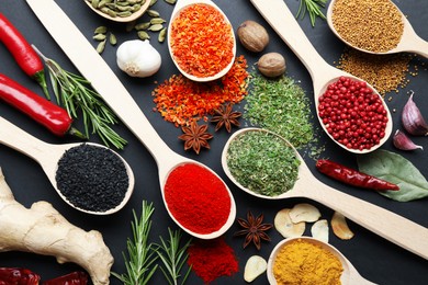 Photo of Different aromatic spices in spoons on black table, flat lay