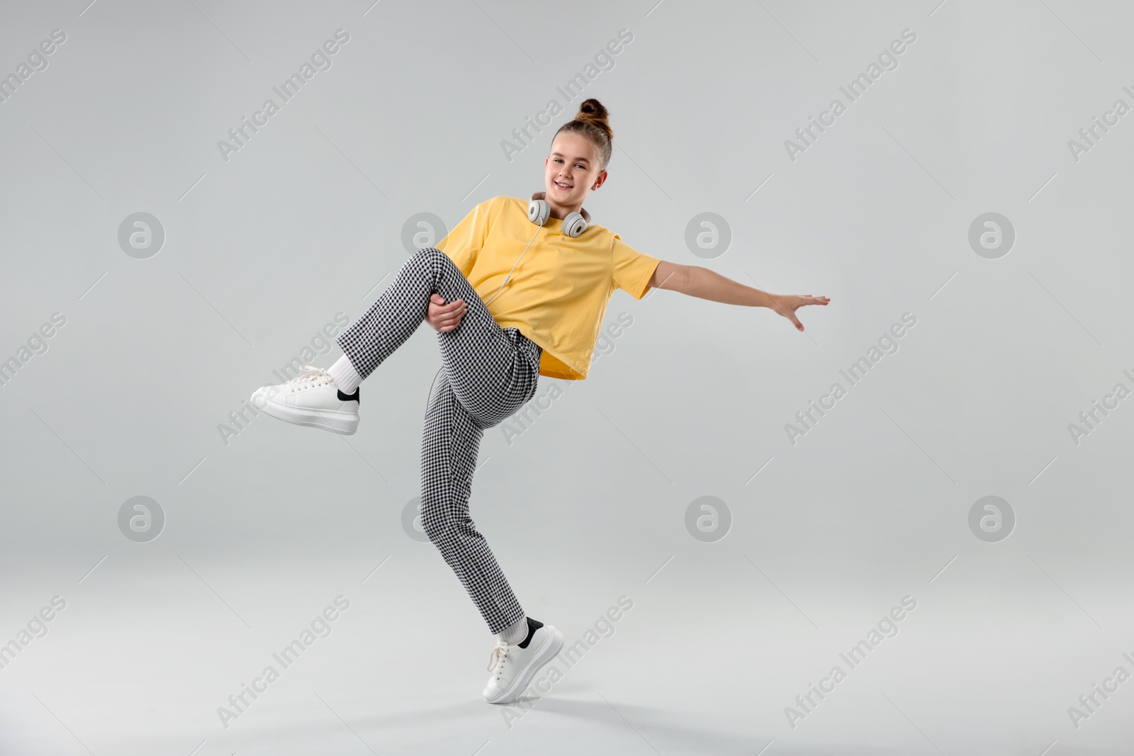 Girl with headphones in stylish clothes dancing on light grey background Photo of Girl with headphones in stylish clothes dancing on light grey background