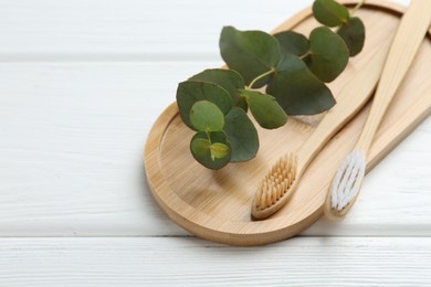 Photo of Bamboo toothbrushes and eucalyptus branch on white wooden table, closeup. Space for text