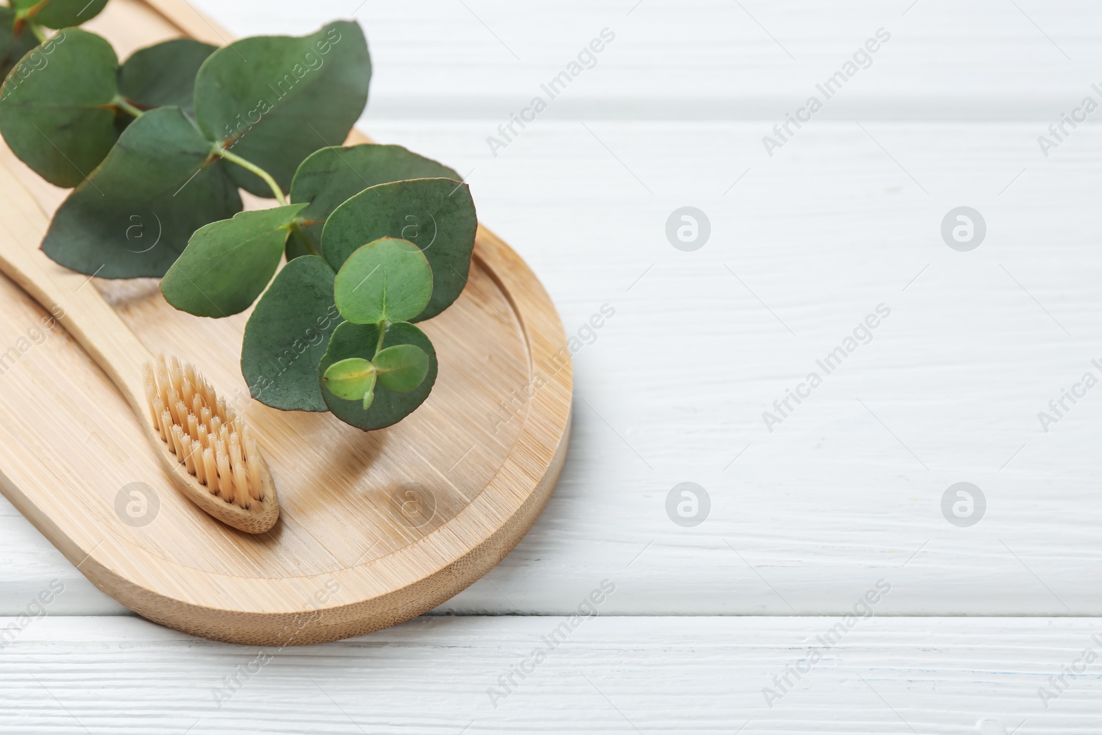 Bamboo toothbrush and eucalyptus branch on white wooden table, closeup. Space for text Photo of Bamboo toothbrush and eucalyptus branch on white wooden table, closeup. Space for text