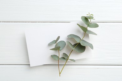 Photo of Blank card and eucalyptus branches on white wooden table, top view