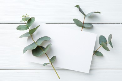 Photo of Blank card and eucalyptus branches on white wooden table, flat lay