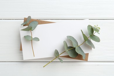 Photo of Blank card and eucalyptus branches on white wooden table, top view
