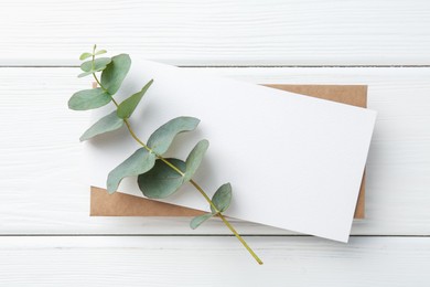 Photo of Blank card and eucalyptus branch on white wooden table, top view