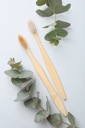 Photo of Bamboo toothbrushes and eucalyptus branches on white background, flat lay