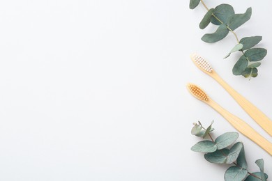 Photo of Bamboo toothbrushes and eucalyptus branches on white background, flat lay. Space for text