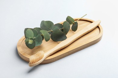 Photo of Bamboo toothbrush and eucalyptus branch on white background, closeup