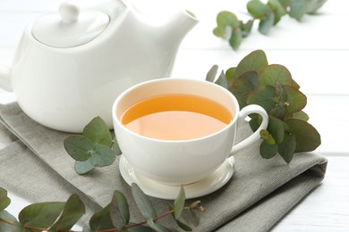 Photo of Aromatic tea in cup and eucalyptus branches on white wooden table, closeup